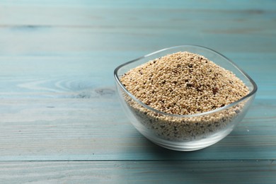 Photo of Raw quinoa seeds in bowl on light blue wooden table, closeup. Space for text