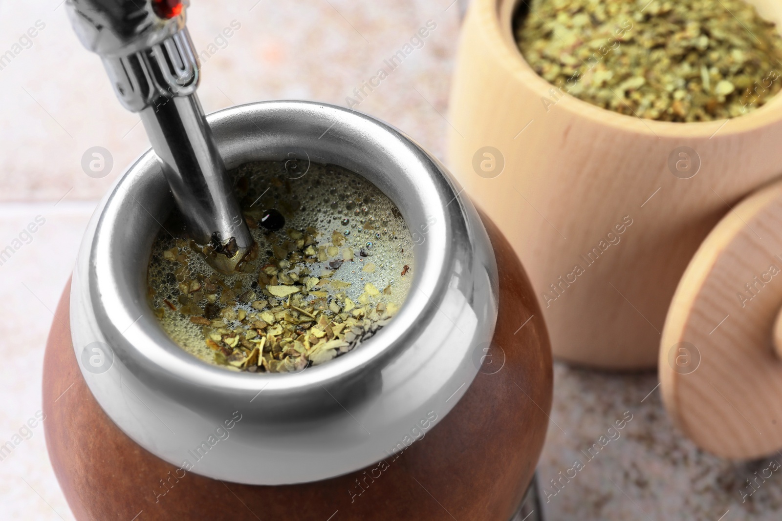 Photo of Calabash with bombilla and jar of mate tea leaves on tiled table, closeup