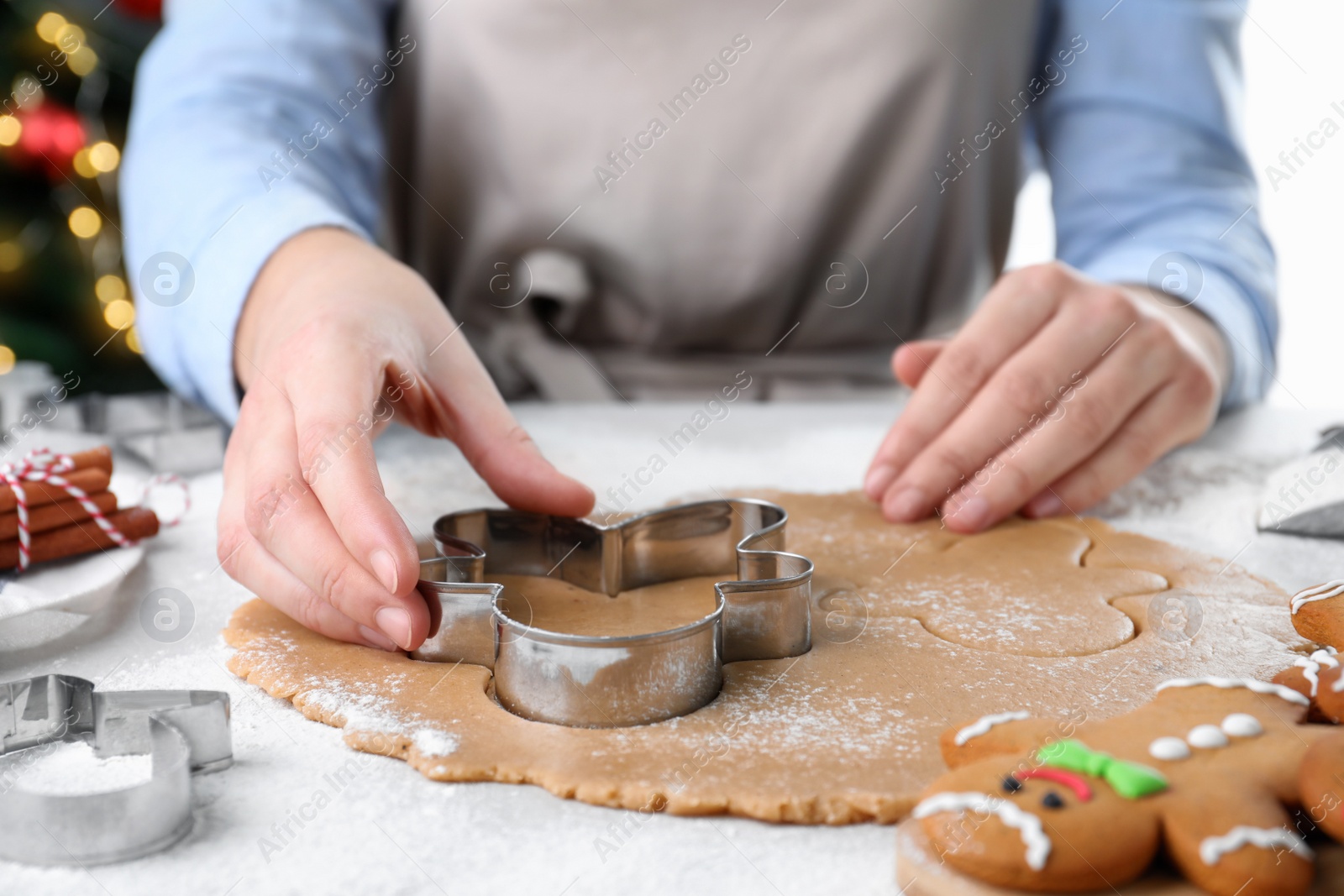 Photo of Woman making Christmas gingerbread man cookies at white table, closeup