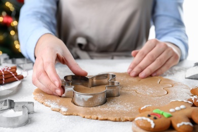 Photo of Woman making Christmas gingerbread man cookies at white table, closeup