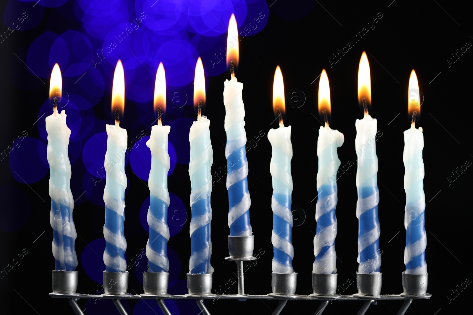 Photo of Hanukkah celebration. Menorah with burning candles against dark background with blurred lights, closeup