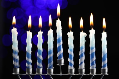 Photo of Hanukkah celebration. Menorah with burning candles against dark background with blurred lights, closeup