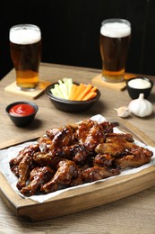 Photo of Tasty chicken wings, sauces, vegetable sticks and glasses of beer on wooden table. Delicious snacks
