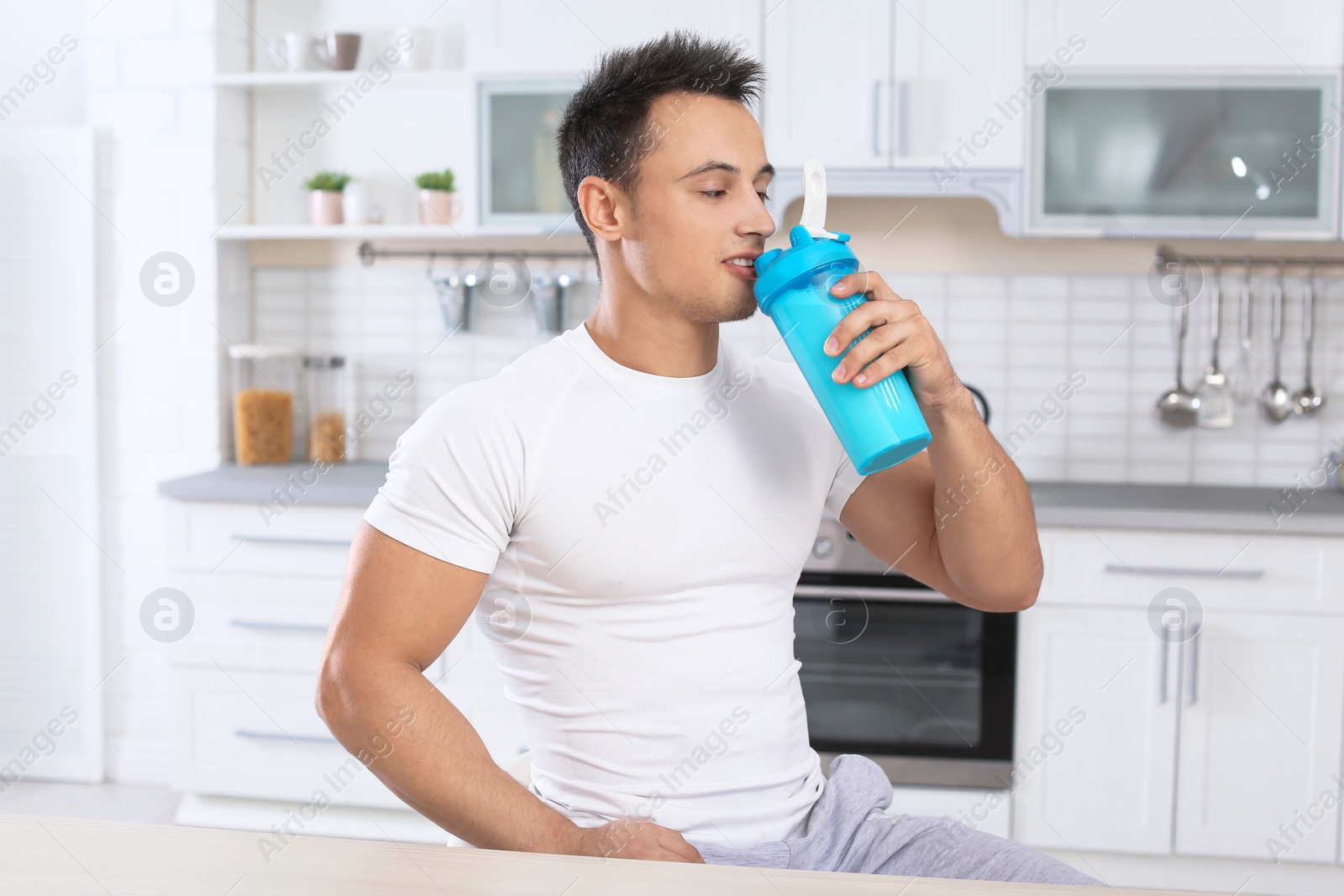 Photo of Young man drinking protein shake in kitchen