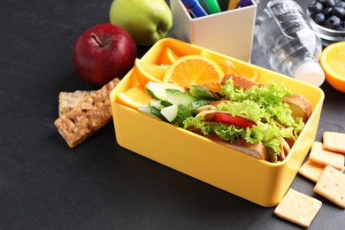 Lunch box with healthy food for schoolchild and markers on black textured table