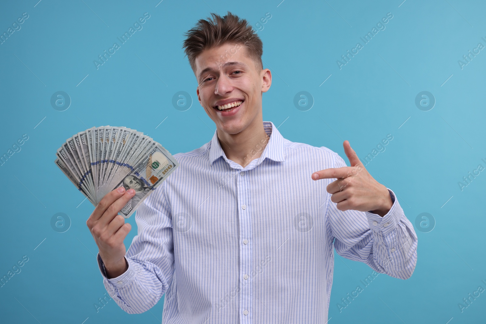 Photo of Happy man pointing at dollar banknotes on light blue background