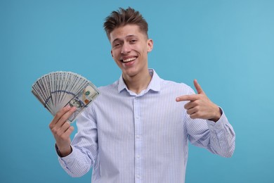 Happy man pointing at dollar banknotes on light blue background