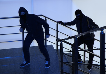 Photo of Men in masks with knife on stairs indoors. Dangerous criminals