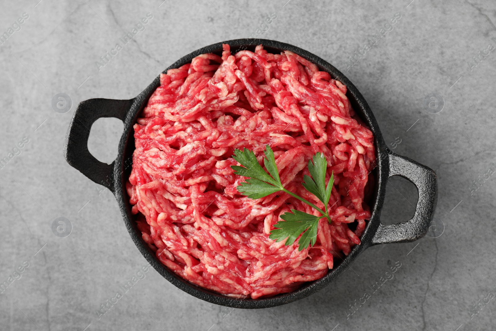 Photo of Raw ground meat and parsley in bowl on grey table, top view