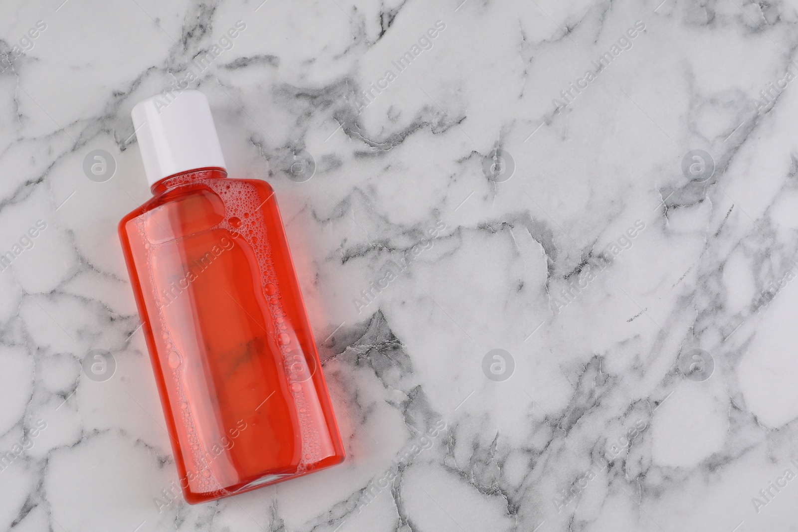 Photo of Fresh mouthwash in bottle on white marble table, top view. Space for text