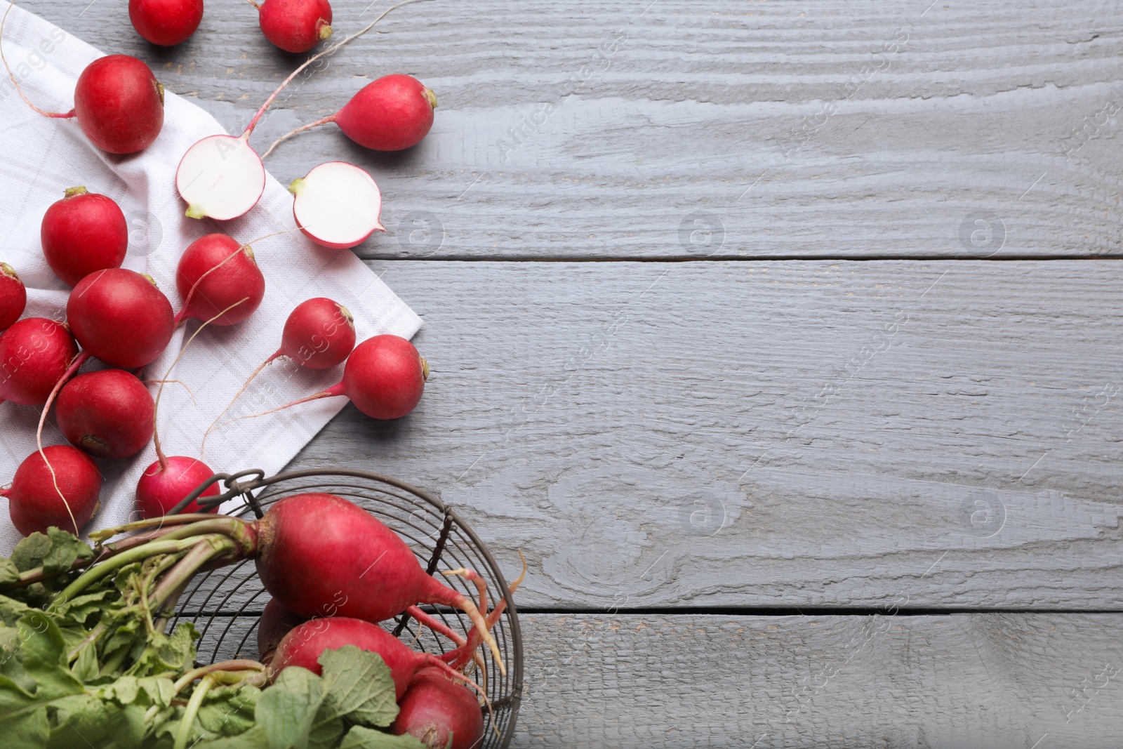 Photo of Metal basket with fresh ripe radishes on grey wooden table, flat lay. Space for text