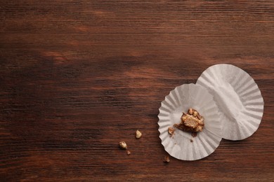 Paper cups with piece of chocolate candy on wooden table, flat lay. Space for text