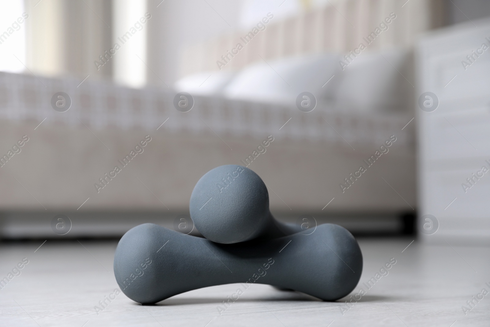 Photo of Grey dumbbells on floor indoors. Fitness at home