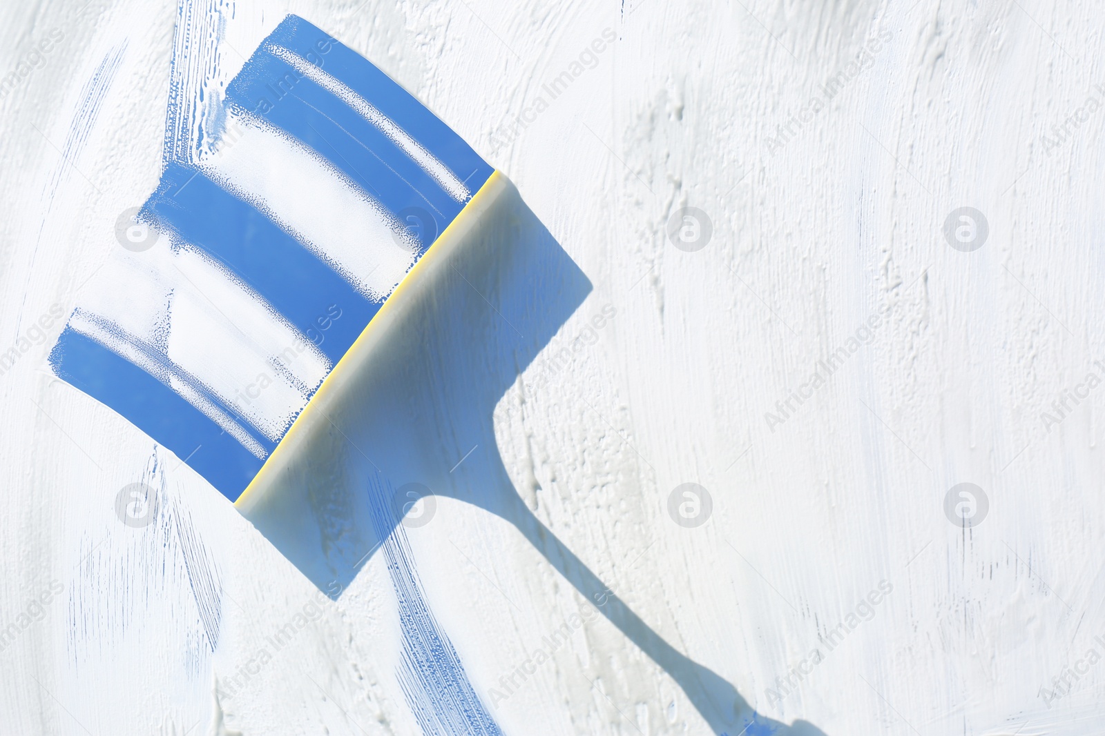 Photo of Squeegee and cleaning foam on glass, closeup