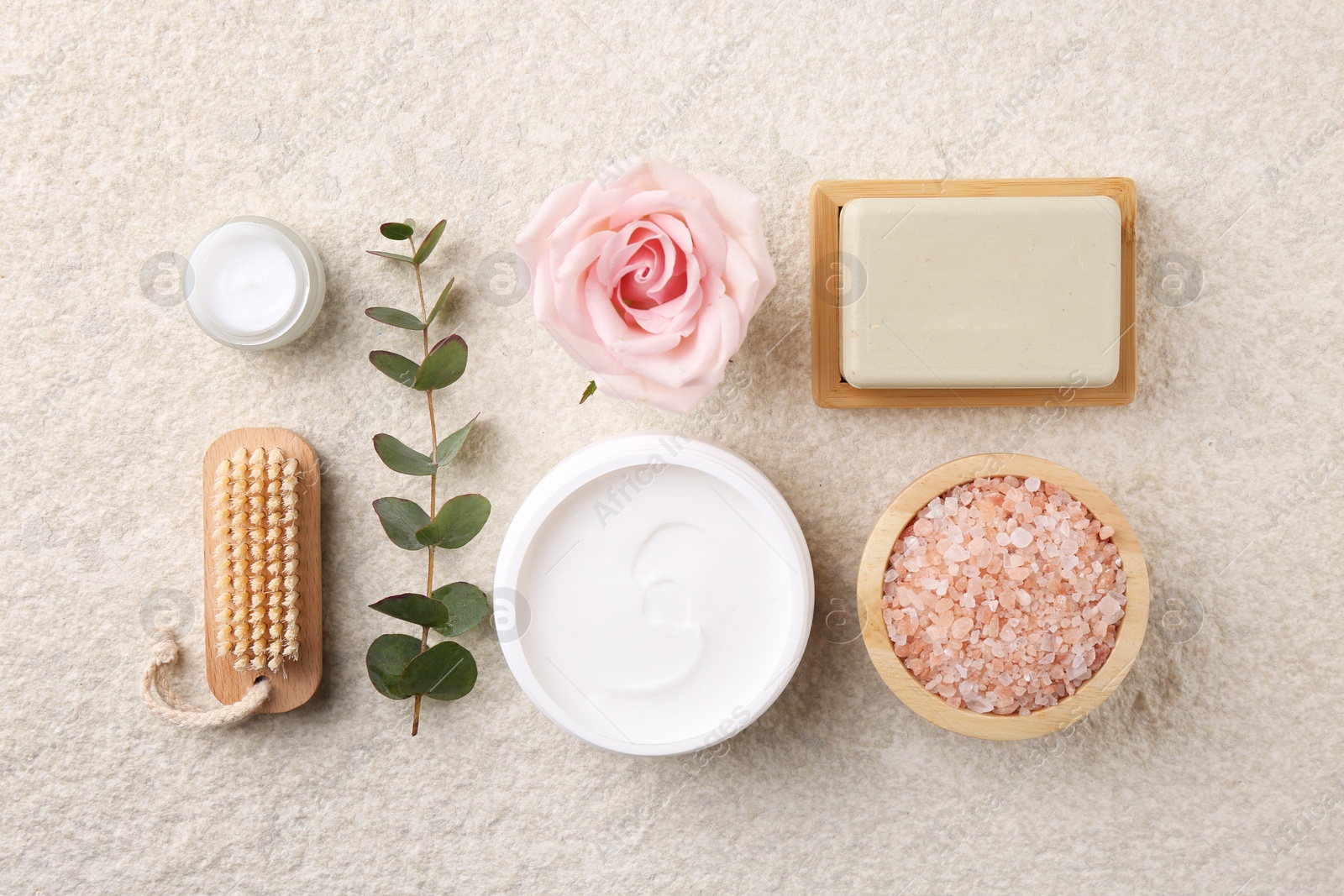 Photo of Flat lay composition with moisturizing cream in open jar and other body care products on light textured table