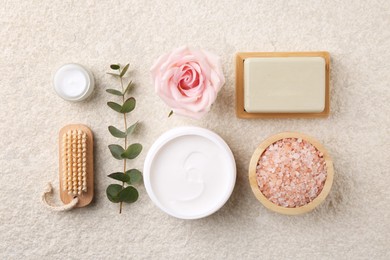 Flat lay composition with moisturizing cream in open jar and other body care products on light textured table