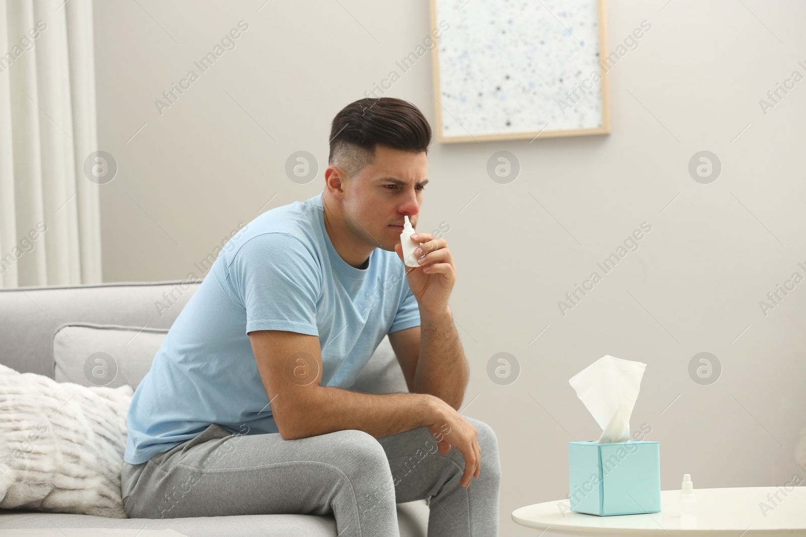 Photo of Ill man using nasal spray on sofa at home