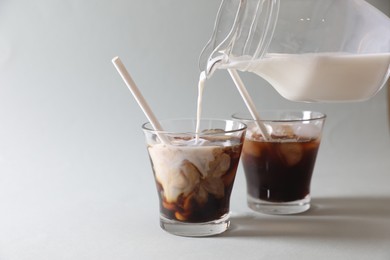 Photo of Pouring milk into glass with refreshing iced coffee on grey background, closeup. Space for text