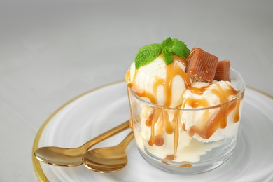 Delicious ice cream with caramel sauce, candies and mint served on light grey table