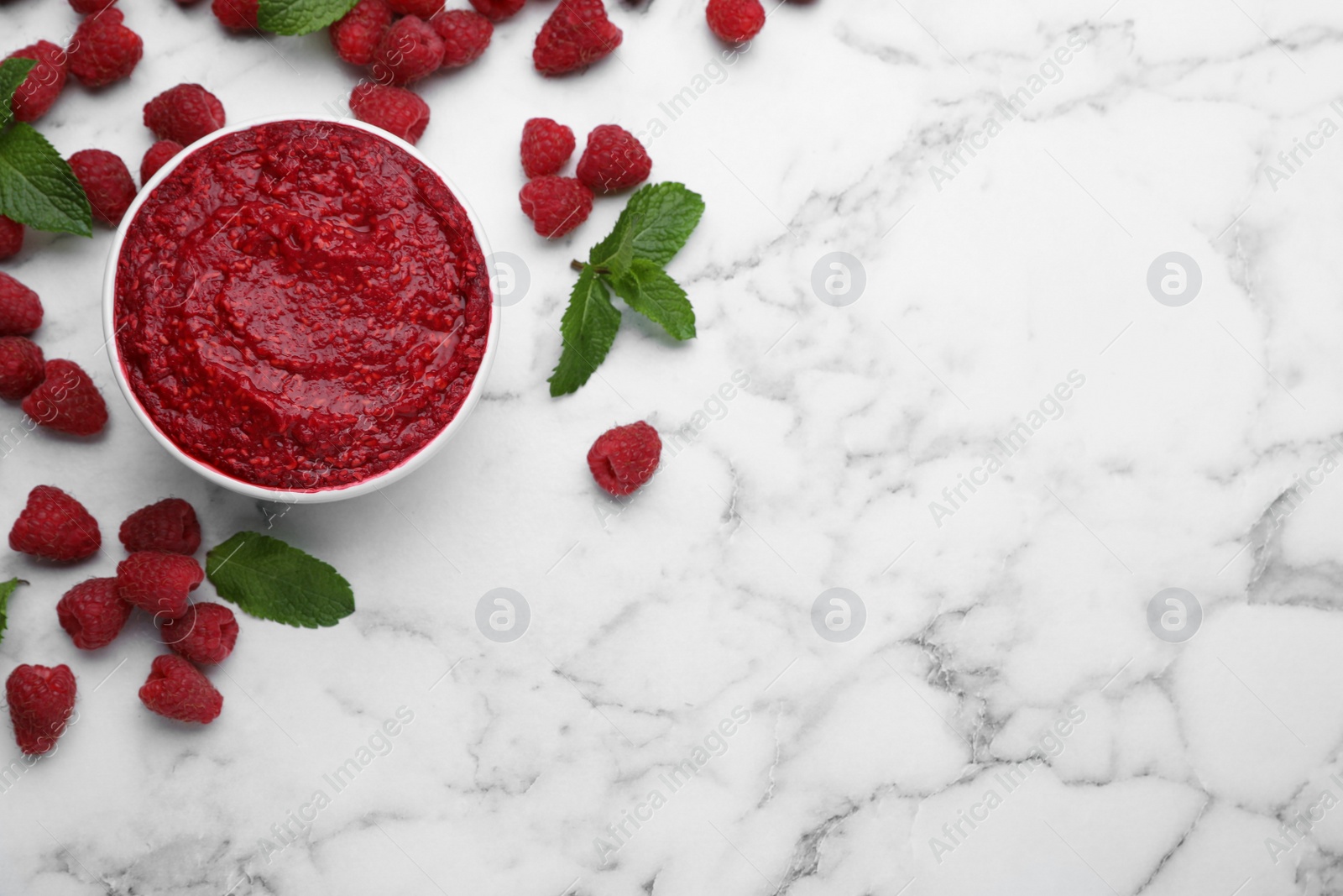 Photo of Raspberry puree in bowl and fresh berries with mint on white marble table, flat lay. Space for text