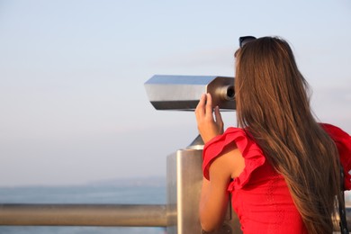 Young woman looking through tourist viewing machine at observation deck, space for text