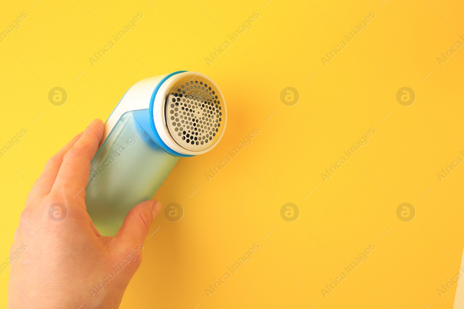 Photo of Woman holding modern fabric shaver on yellow background, closeup. Space for text