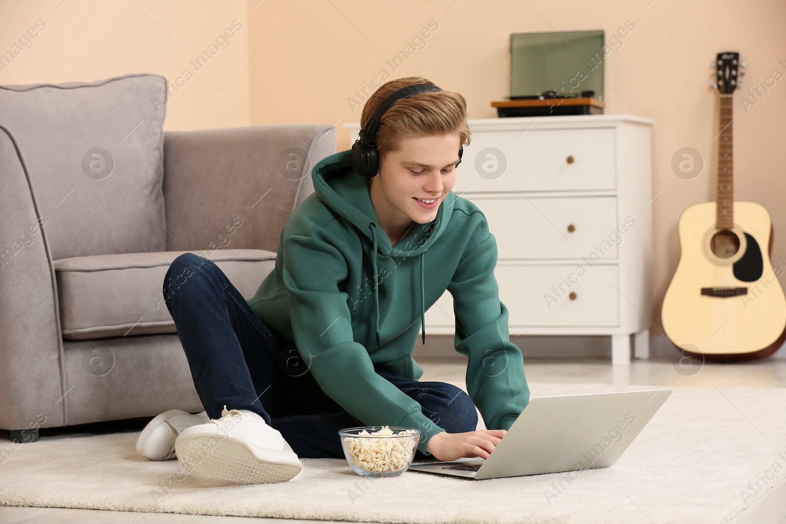 Photo of Teenage boy with headphones and popcorn using laptop at home