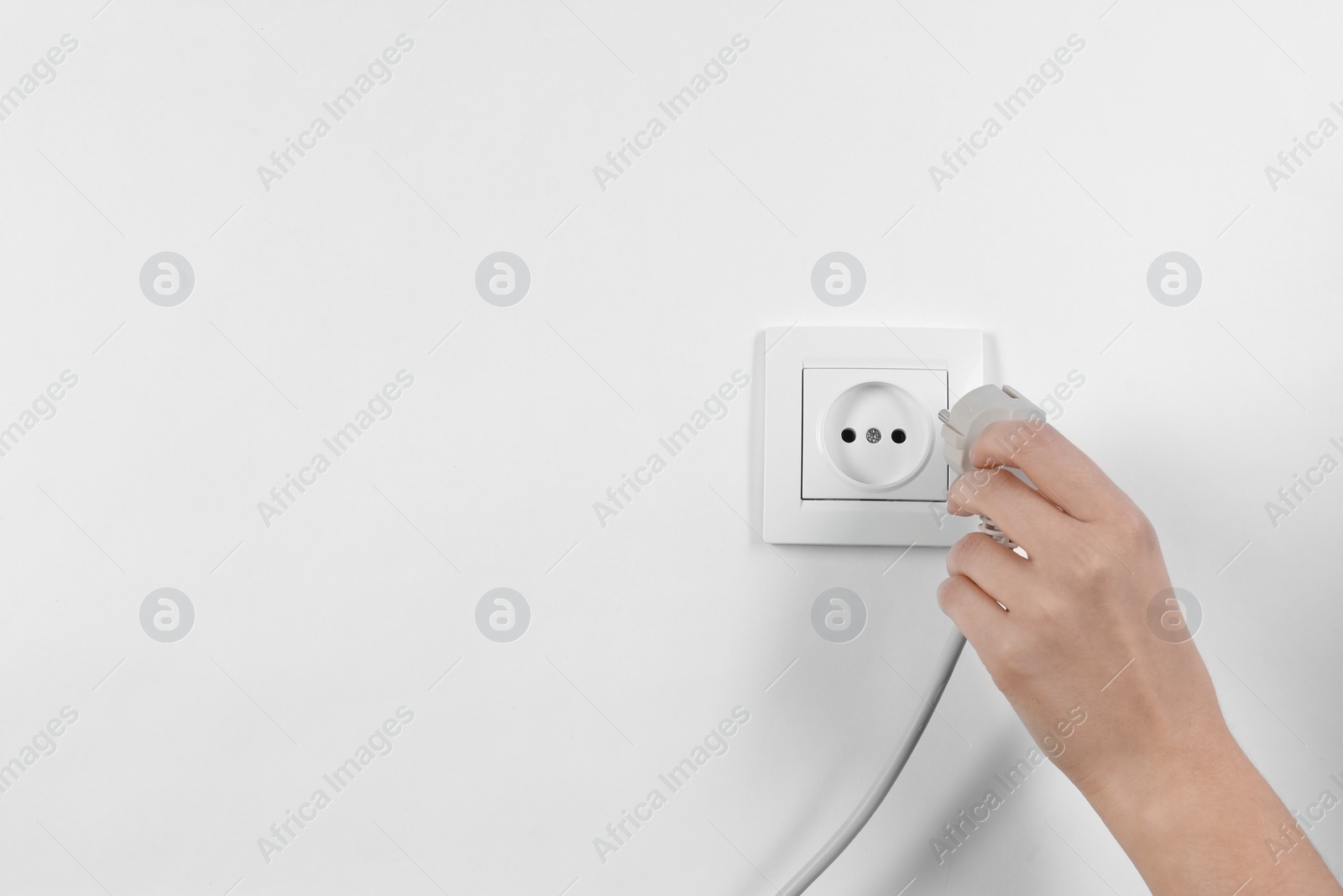 Photo of Woman putting plug into power socket on white background, closeup. Electrician's equipment