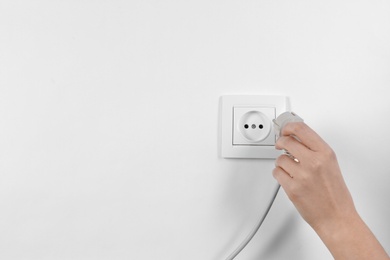 Woman putting plug into power socket on white background, closeup. Electrician's equipment