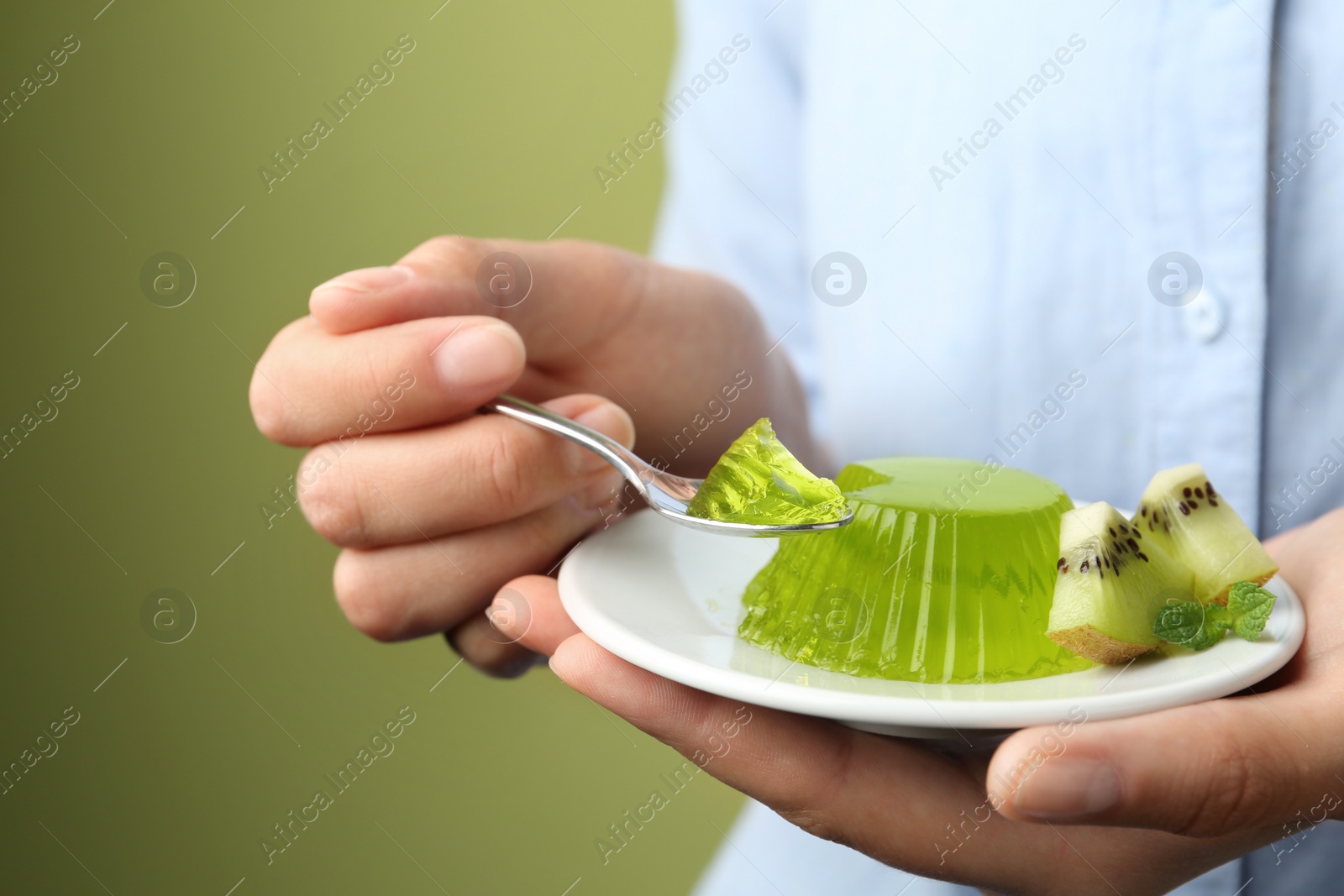 Photo of Young woman eating tasty kiwi jelly on green background, closeup