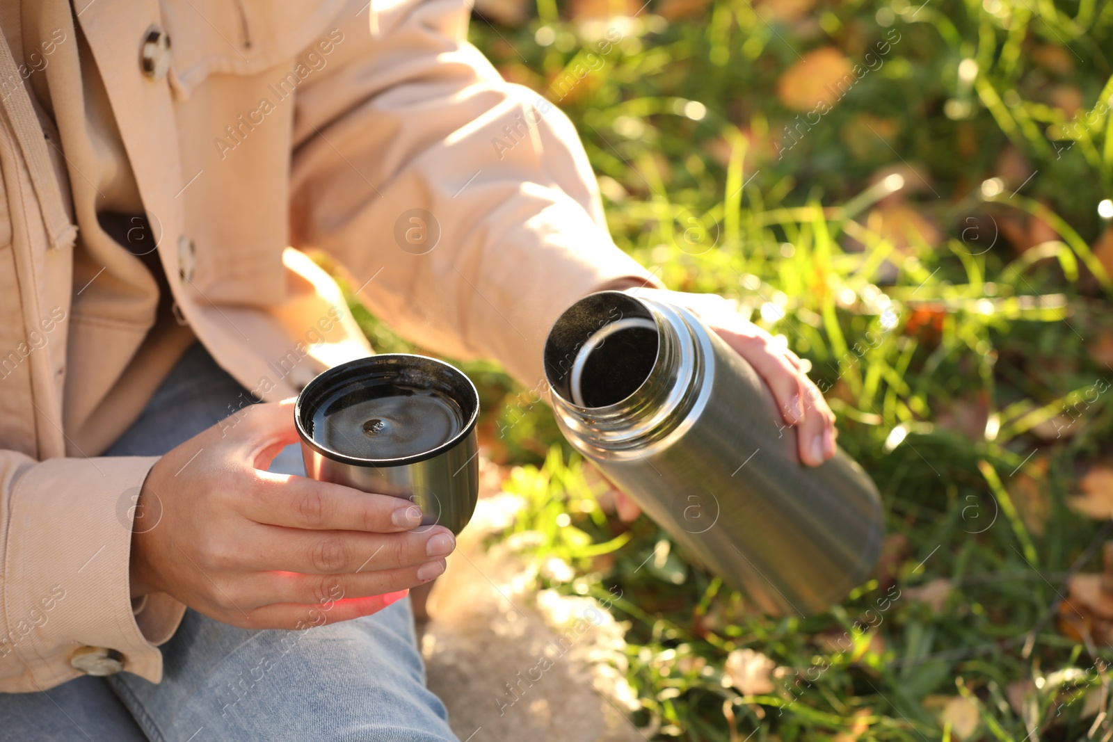 Photo of Woman with thermos and cup lid on green grass outdoors, closeup