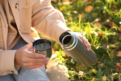 Photo of Woman with thermos and cup lid on green grass outdoors, closeup