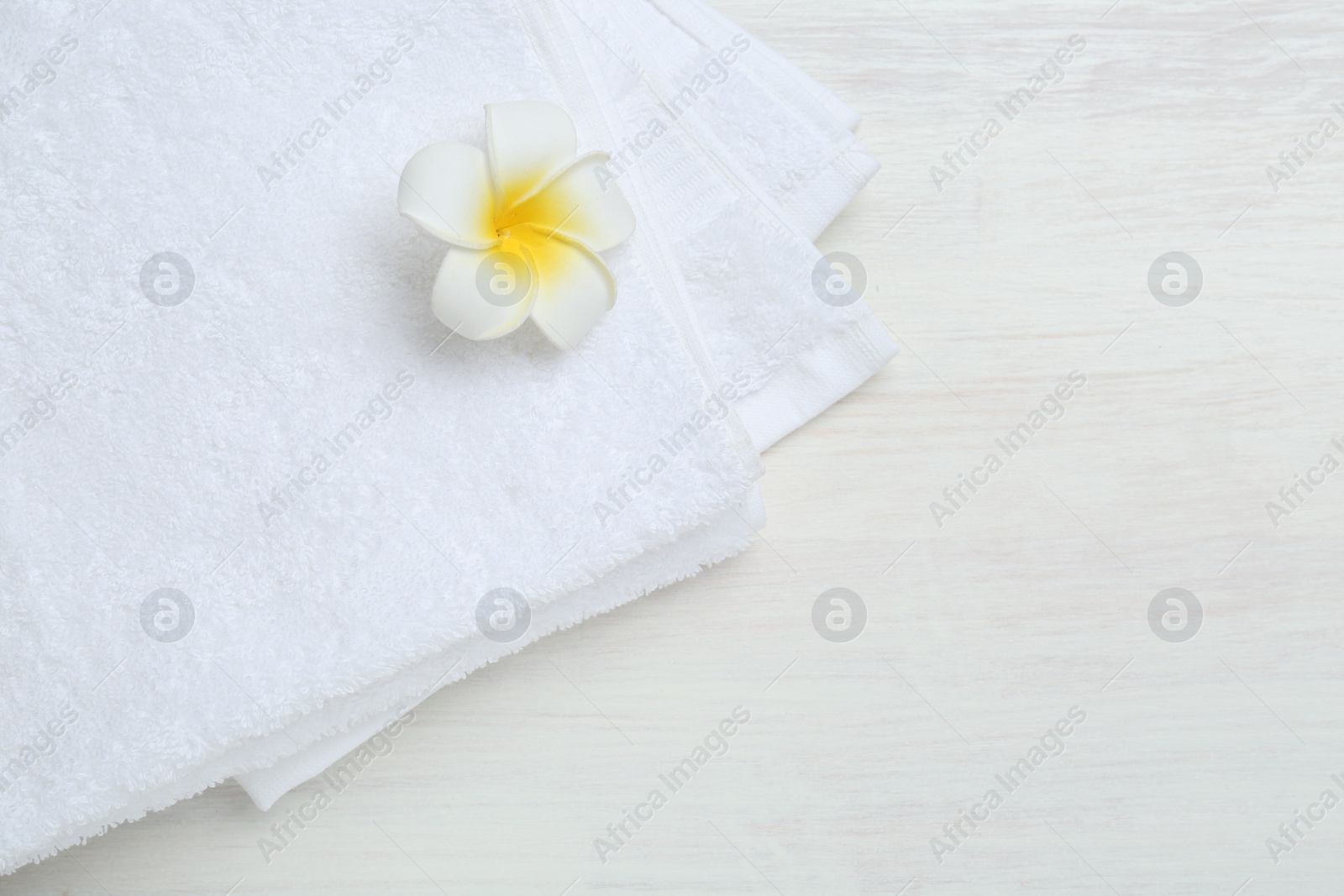 Photo of White terry towels and plumeria flower on light wooden table, top view. Space for text