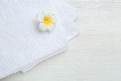 White terry towels and plumeria flower on light wooden table, top view. Space for text