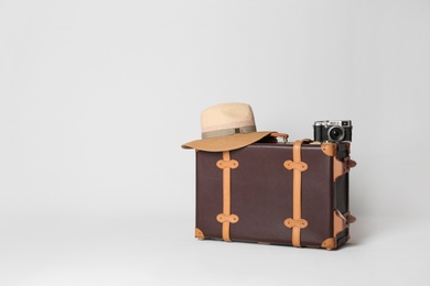 Photo of Vintage travel suitcase with hat and camera on light grey background, space for text. Summer vacation