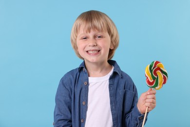 Photo of Happy little boy with colorful lollipop swirl on light blue background