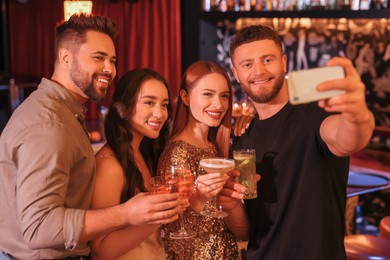 Happy friends with cocktails taking selfie together in bar