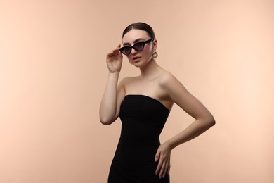 Photo of Portrait of beautiful young woman with sunglasses on beige background