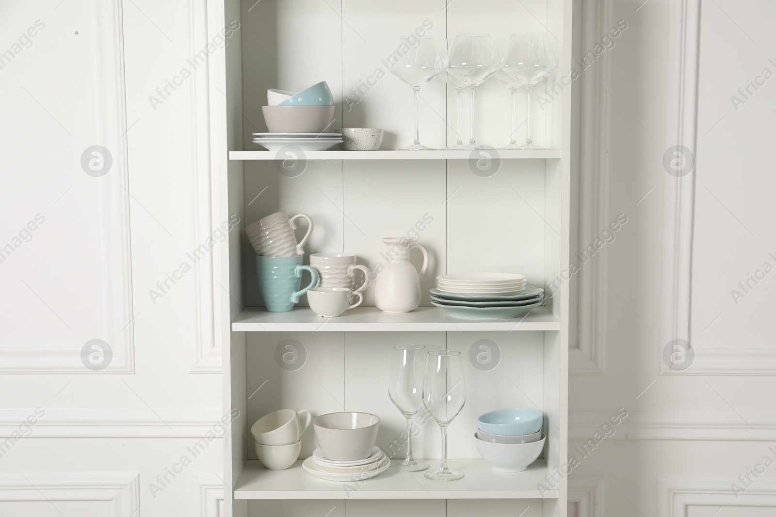 Photo of Different clean dishware and glasses on shelves in cabinet indoors