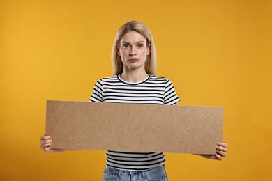 Photo of Woman holding blank cardboard banner on orange background, space for text