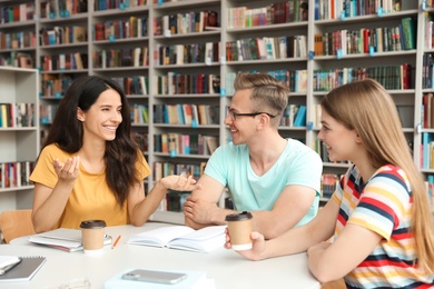 Photo of Young people discussing group project at table in library