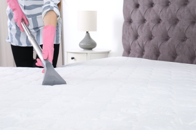 Woman disinfecting mattress with vacuum cleaner, closeup. Space for text