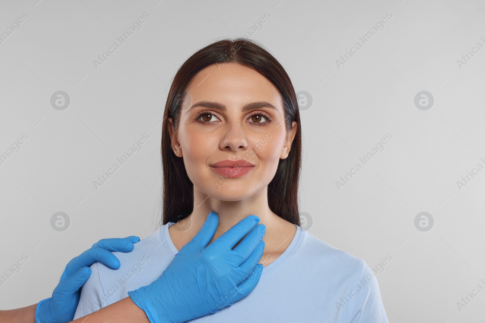 Photo of Endocrinologist examining thyroid gland of patient on light grey background, closeup