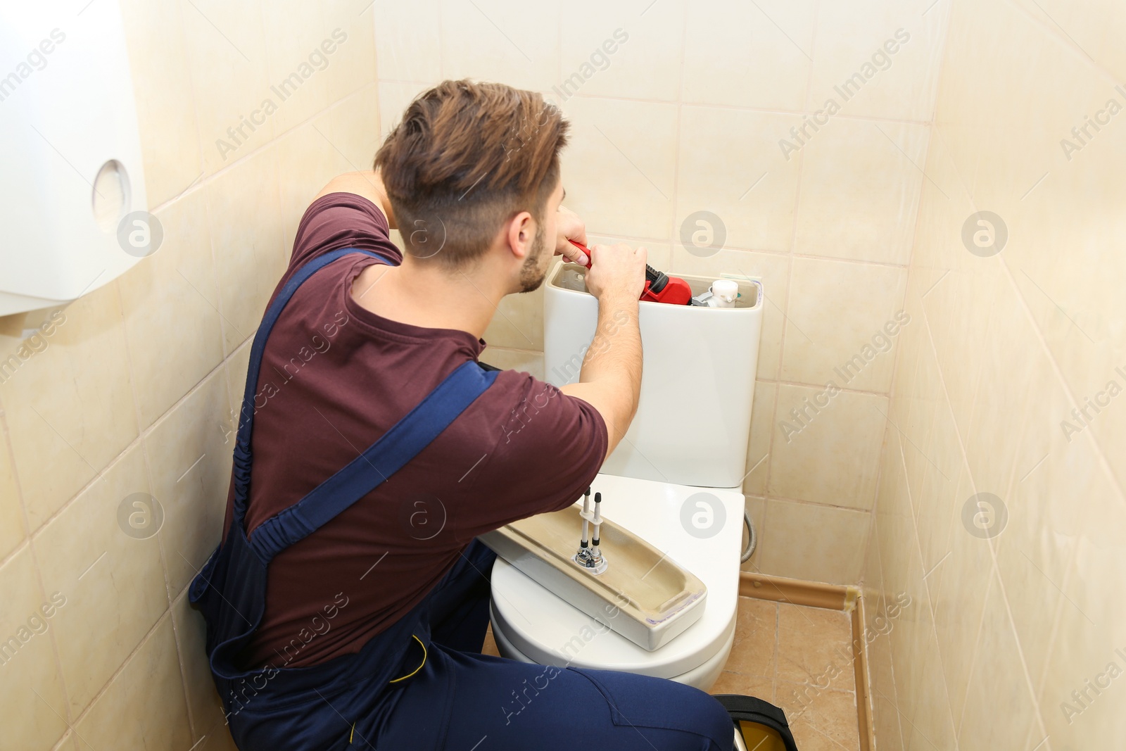 Photo of Male plumber repairing toilet tank in bathroom. Space for text