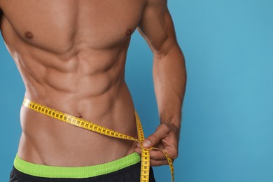 Photo of Shirtless man with slim body and measuring tape around his waist on light blue background, closeup