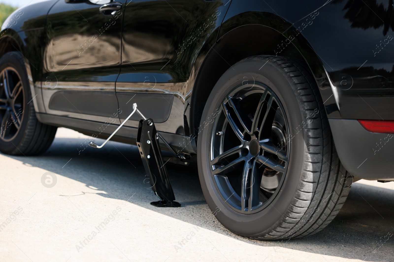 Photo of Car lifted by scissor jack on roadside outdoors. Tire puncture