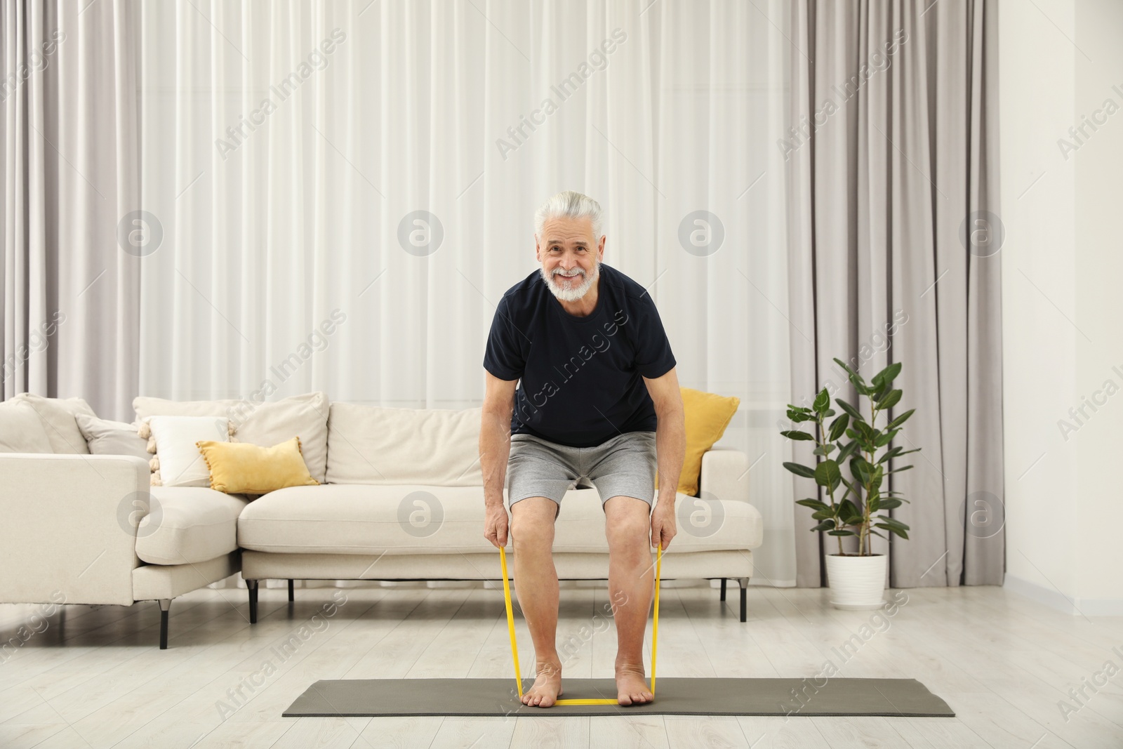 Photo of Senior man doing exercise with fitness elastic band on mat at home