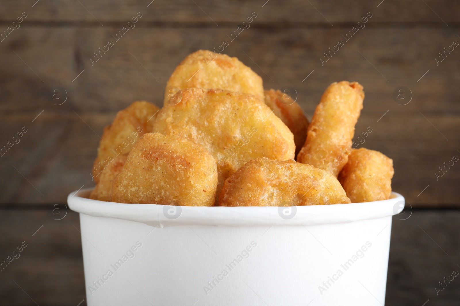 Photo of Bucket with tasty chicken nuggets on wooden background, closeup