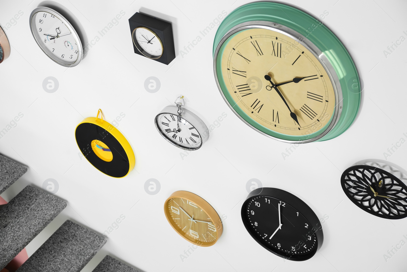 Photo of Many different clocks hanging on white wall. Time of day