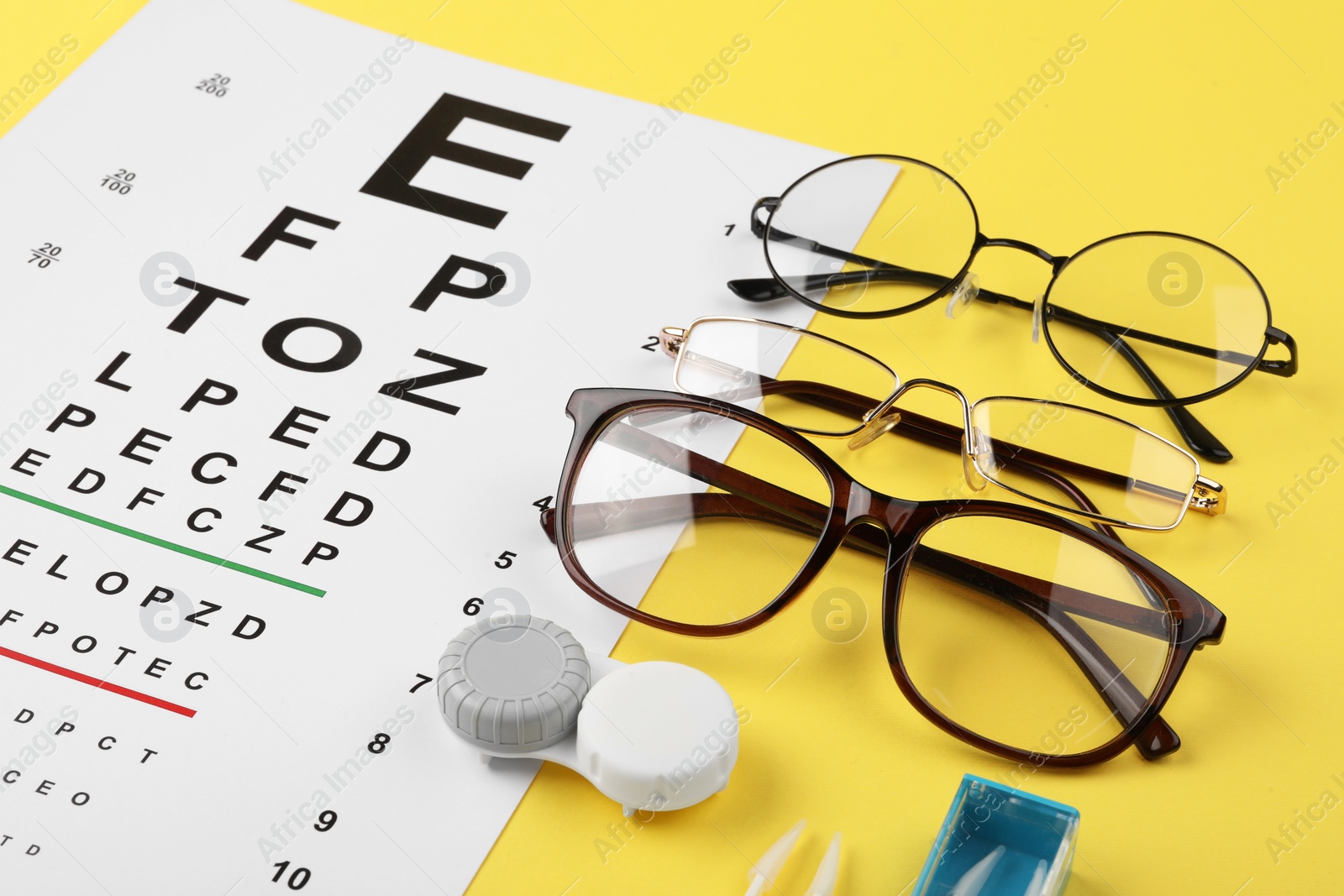 Photo of Vision test chart, glasses and lenses on yellow background, closeup